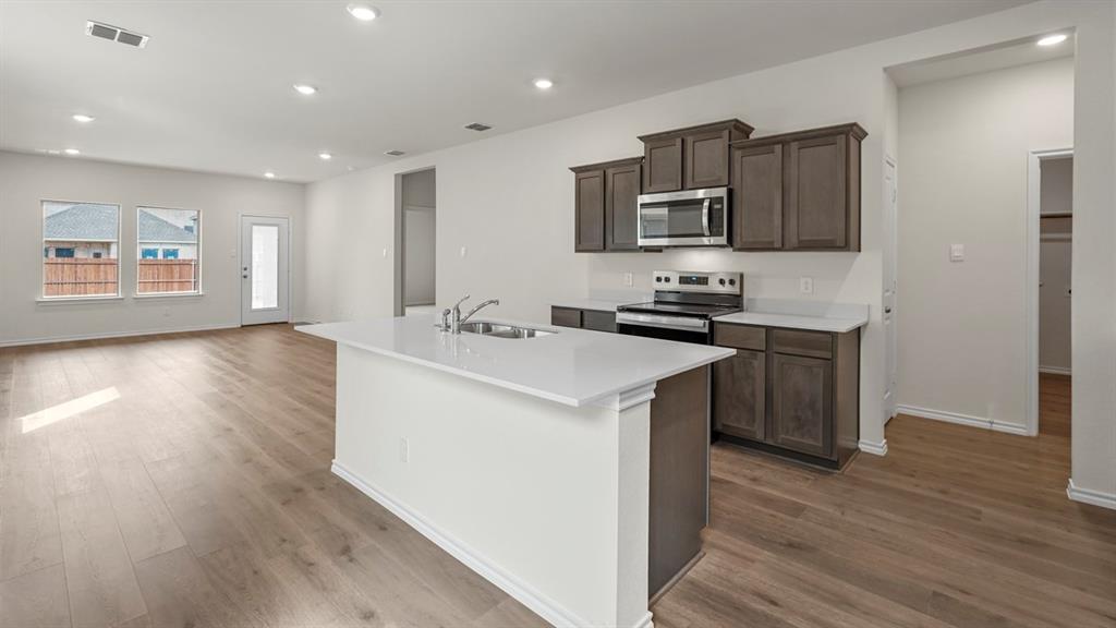 Open-concept kitchen featuring an island with a sink, wood-finish flooring, recessed lighting, white countertops, and dark wood cabinetry