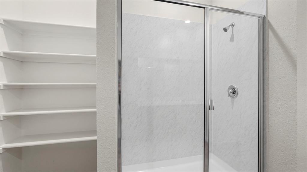 Shower enclosure with clear glass doors and a white marble-look surround, featuring a chrome shower head and handle