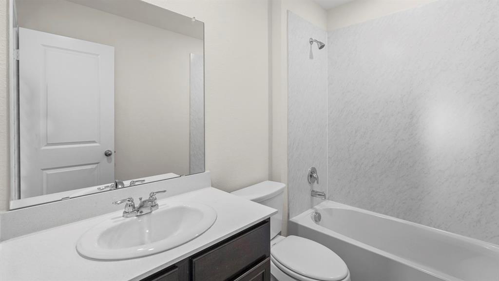 Bathroom featuring a vanity with an integrated sink, polished chrome faucet, full-width mirror, and a tub-shower combination with a textured surround Bathroom featuring a vanity with an integrated sink, polished chrome faucet, full-width mirror, and a tub-shower combination with a textured surround
