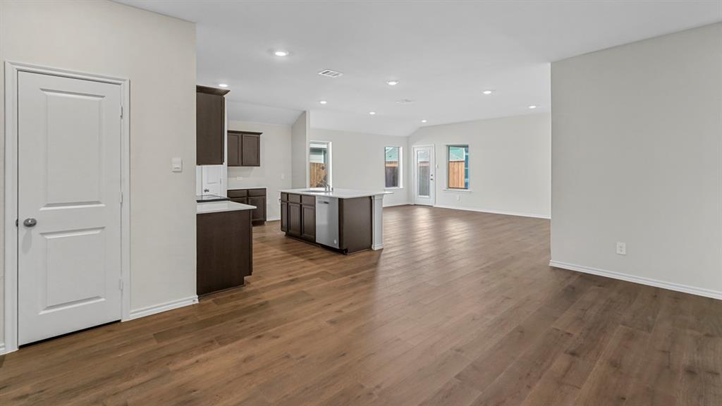 Open-concept living space featuring wood-finish flooring throughout, dark cabinetry with stainless steel appliances, recessed ceiling lighting, and abundant natural light from multiple windows