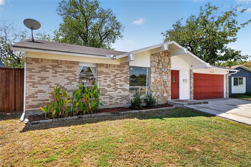 Brick and stone exterior with a prominent red garage door, a concrete driveway, and established landscaping