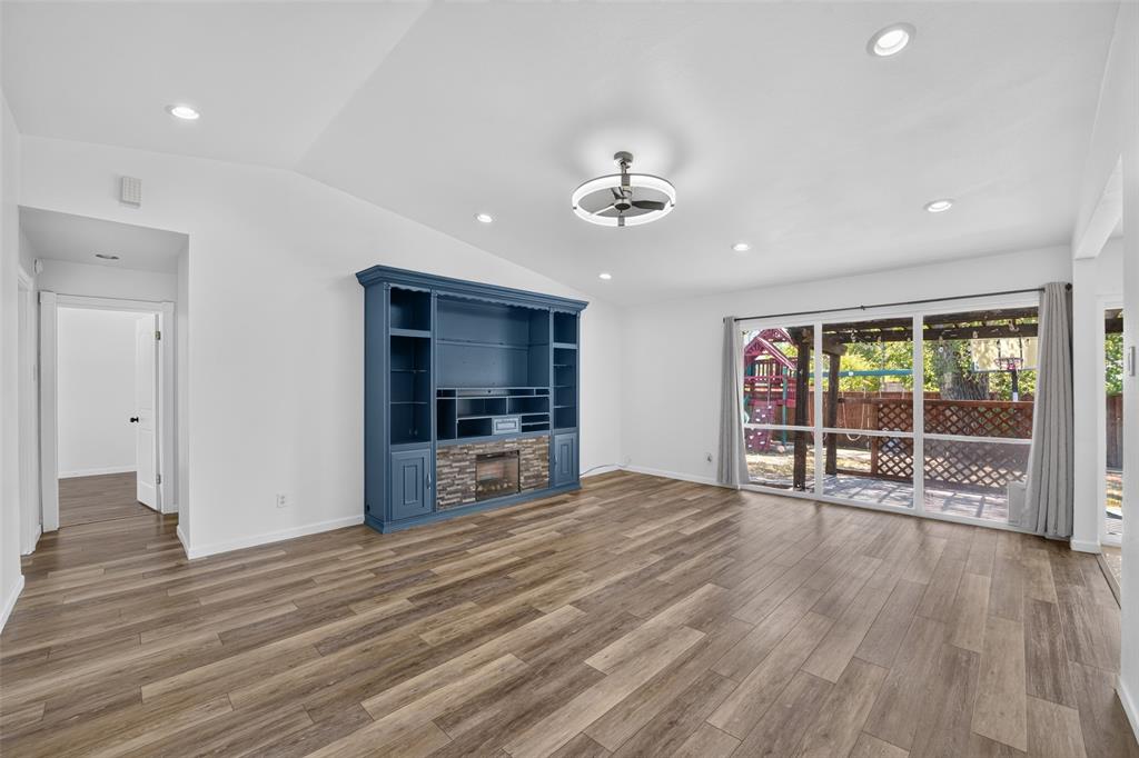 Vaulted ceiling, recessed lighting, wood-finish flooring, built-in entertainment center with stone accent, and sliding glass doors