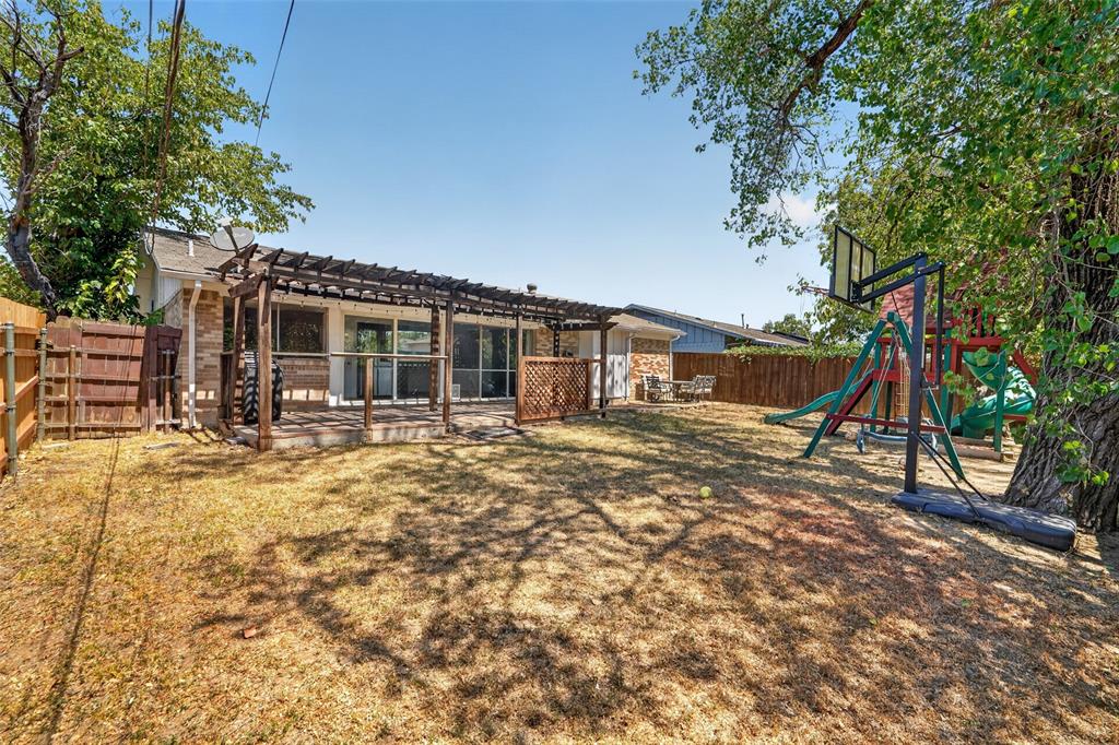 Expansive backyard featuring a wood privacy fence, mature trees, and a pergola-covered patio