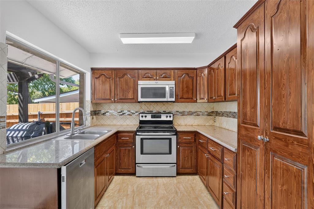 Spacious kitchen featuring extensive wood cabinetry, stainless steel appliances, a double basin sink, and a large window
