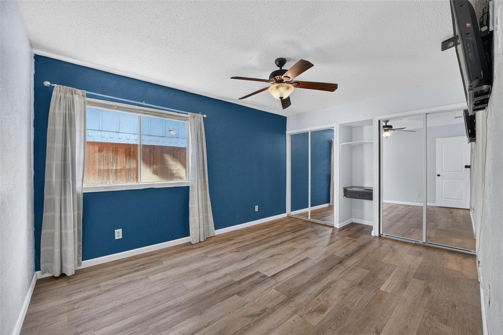Wood-finish flooring, ceiling fan with integrated lighting, window with white trim, and mirrored closet doors