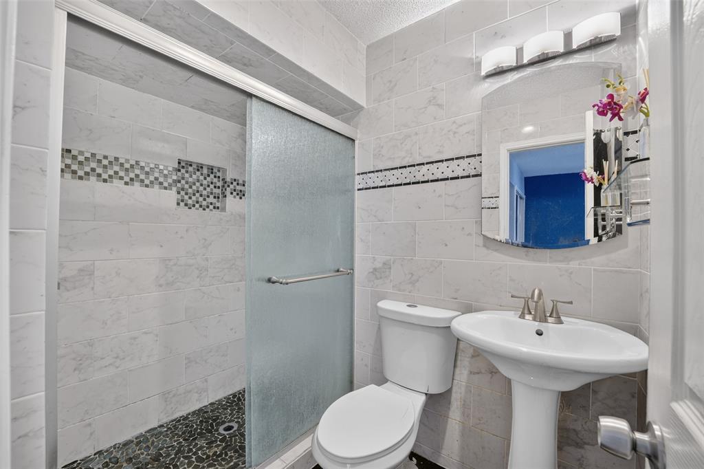 Shower with sliding glass enclosure, mosaic tile accent, and pebble-finish floor