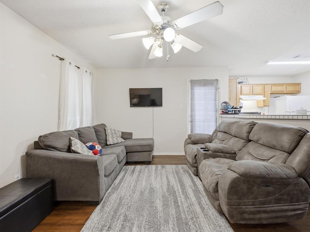Spacious living area featuring wood-finish flooring, ceiling fan with integrated lighting, and white walls