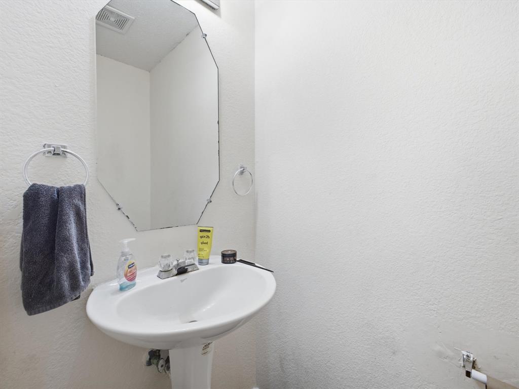 Pedestal sink with chrome faucet, octagonal wall mirror, and chrome towel rings