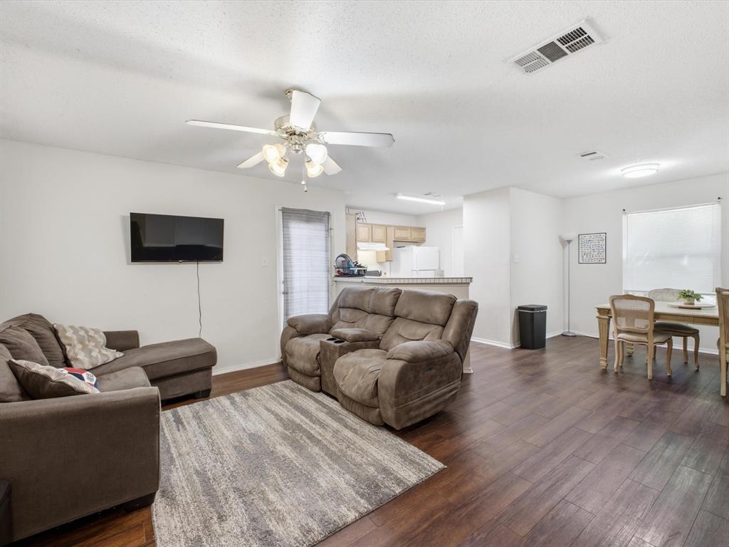 Wood-finish flooring throughout, white walls, and a ceiling fan with integrated lighting