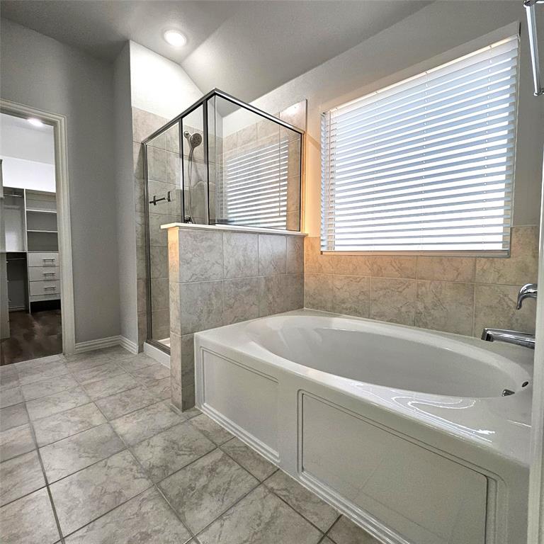Tile flooring, built-in soaking tub, glass-enclosed shower, tiled half-wall, and a window with blinds
