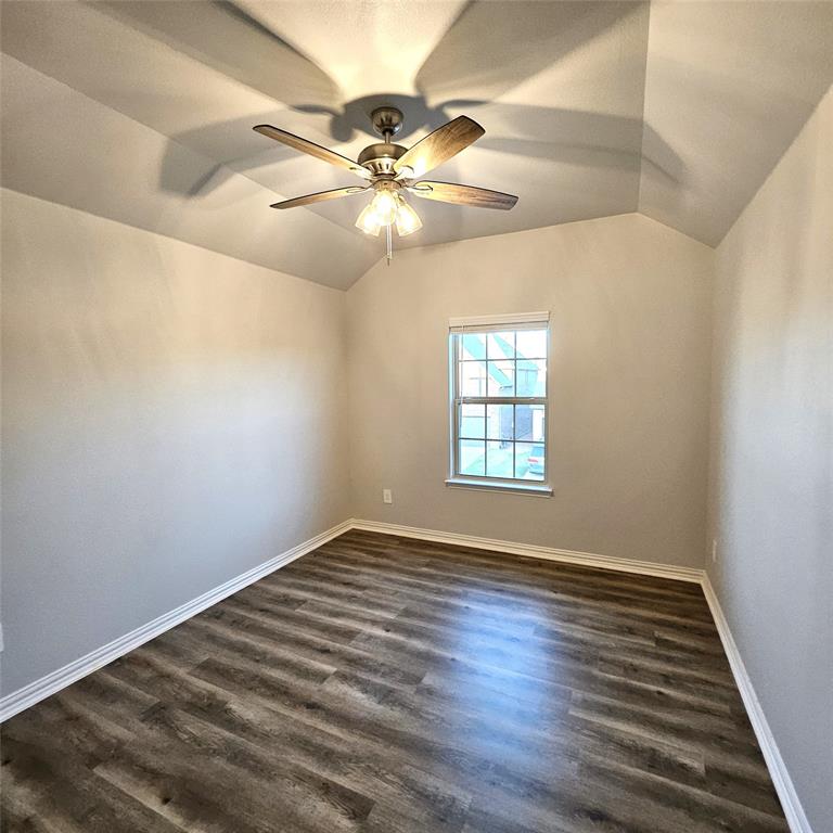 Vaulted ceiling featuring a ceiling fan with integrated lighting, wood-finish flooring, and a window with white trim