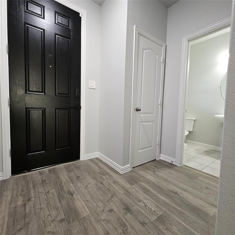 Panel-style entry door, wood-finish flooring, paneled interior door, white baseboards, and a pedestal sink in the powder room