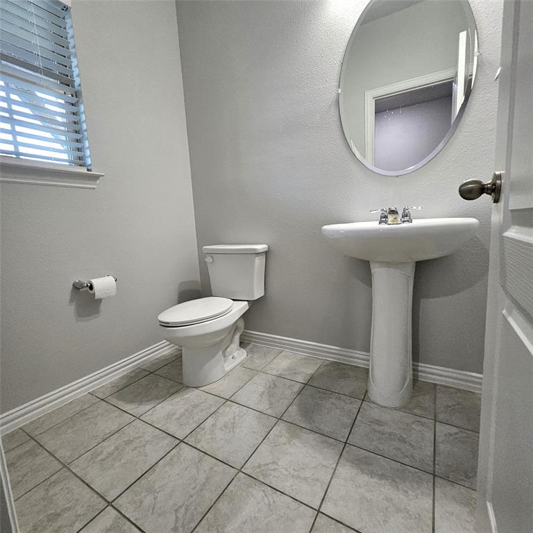 White pedestal sink with chrome faucet, white toilet, oval wall mirror, and tile flooring