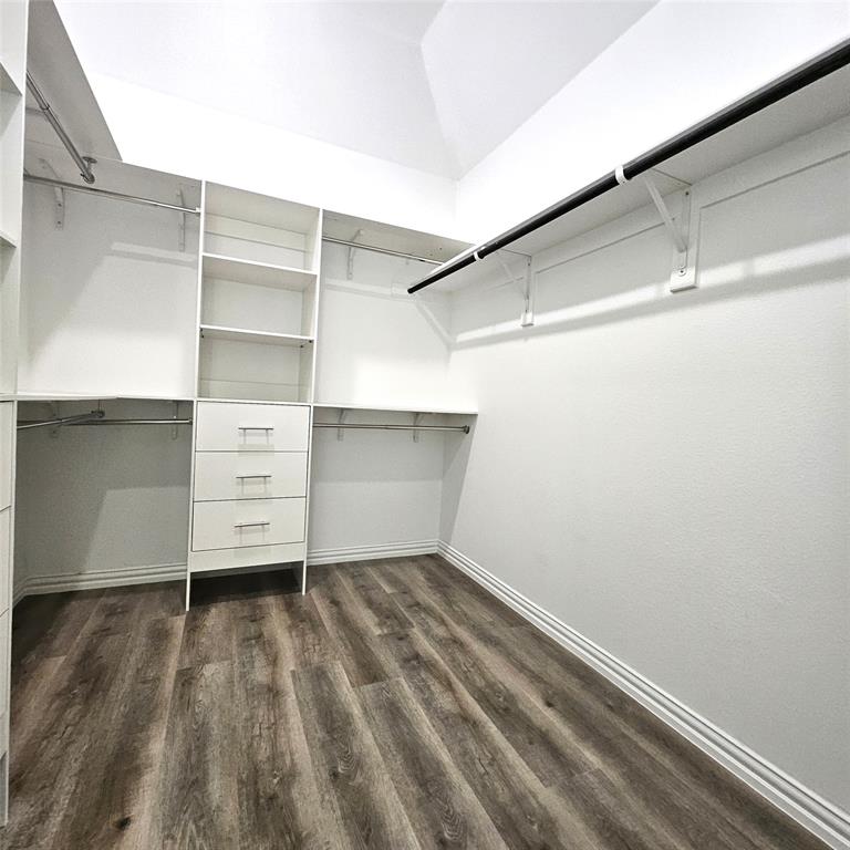 Wood-finish flooring, white built-in shelving, multiple hanging rods, three built-in drawers, and white walls