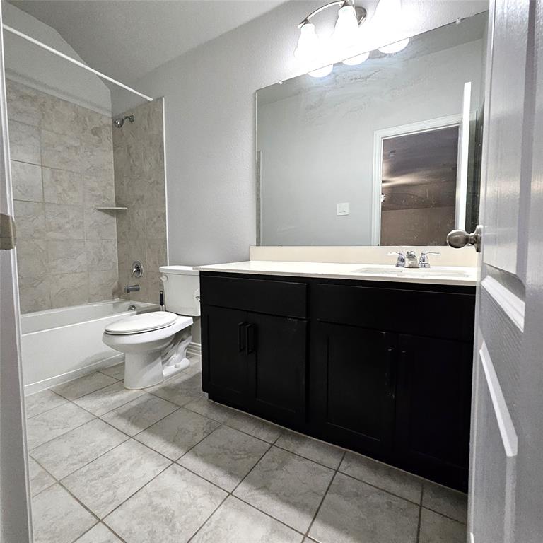 Bathroom featuring a vanity with dark cabinetry and light-toned countertop, a large wall-mounted mirror, a tub/shower combination with tiled surround, and tiled flooring
