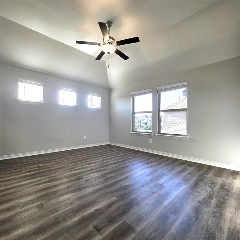 Vaulted ceiling with a ceiling fan, wood-finish flooring, and multiple windows