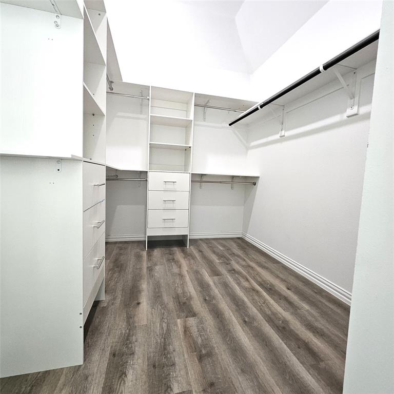 Walk-in closet featuring built-in shelving, integrated drawers, multiple hanging rods, and wood-finish flooring