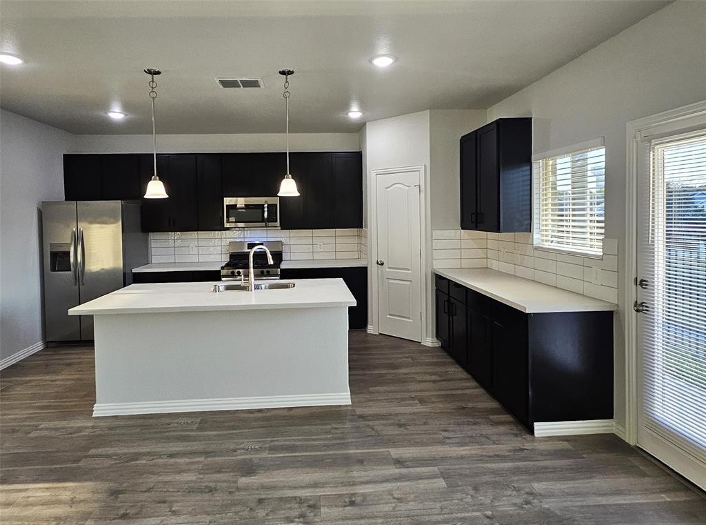 Kitchen featuring a center island, stainless steel appliances, dark cabinetry, light countertops, and wood-finish flooring