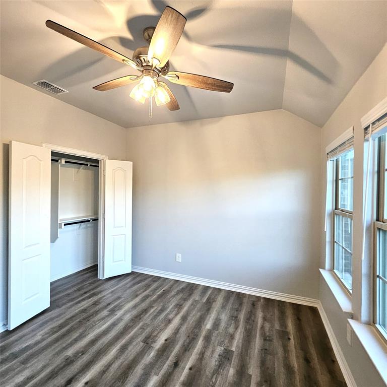 Vaulted ceiling with an attached ceiling fan and light fixture, wood-finish flooring, and a built-in closet with double doors