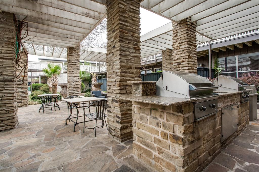 Outdoor entertainment area featuring a stone patio, stone-clad columns, a pergola, and a built-in barbecue station with stainless steel grills and granite-look countertops