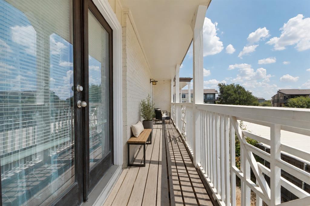 Private balcony with wood-finish decking, white painted brick exterior, and white architectural railings