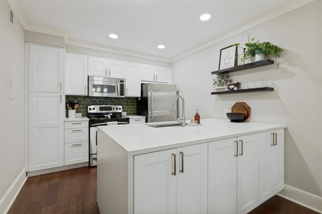 White shaker cabinetry paired with stainless steel appliances, a center island featuring an undermount sink, recessed lighting, and wood-finish flooring