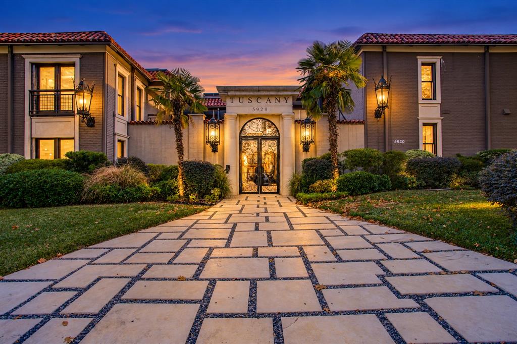 Paver walkway with gravel accents leading to a main entrance featuring an arched doorway, ornate glass and metal doors, and prominent wall sconces