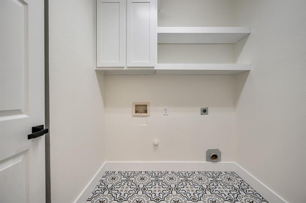 White shaker-style cabinetry, open shelving, white walls, black door hardware, and patterned floor tiling