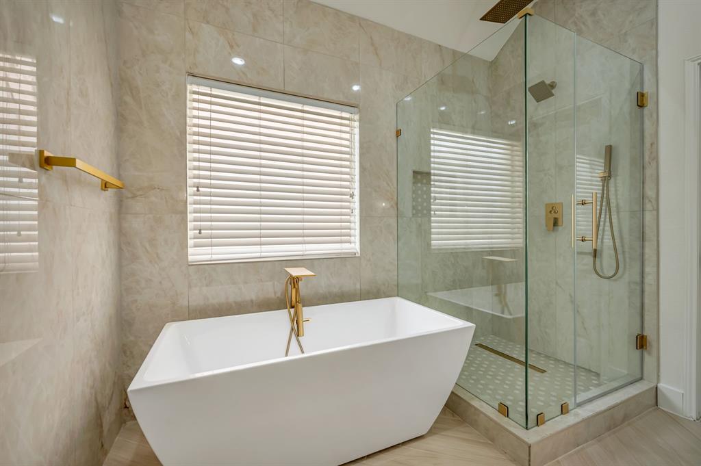 Freestanding soaking tub with gold-finish fixtures, a spacious glass-enclosed shower with a built-in bench, and floor-to-ceiling tile surround