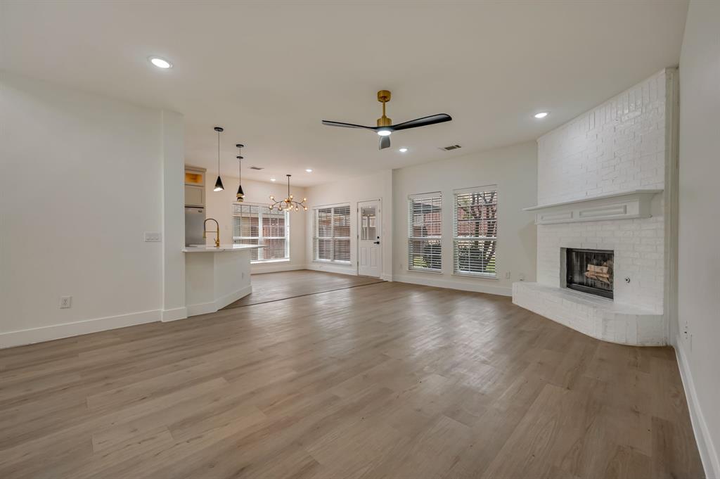 Expansive living area with Luxury Vinyl Plank  flooring, recessed lighting, and a corner brick fireplace with a mantle