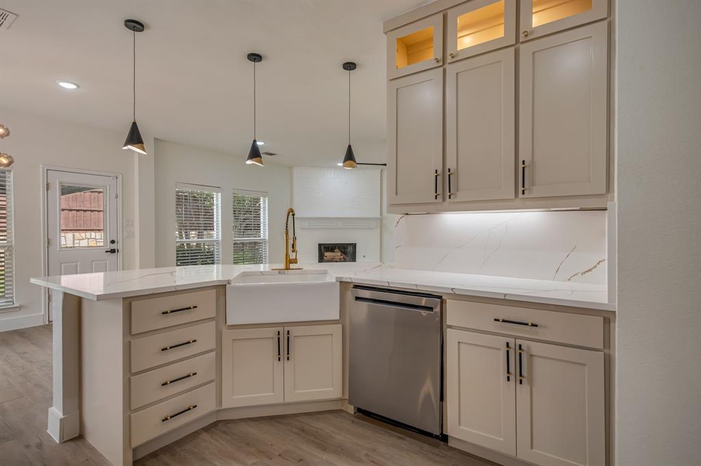 Kitchen with light-toned cabinetry, a farmhouse sink, stainless steel dishwasher, Quartz countertops with gold veining, and pendant lighting