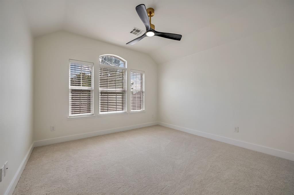 Vaulted ceiling, arched window detail, light-colored carpeting, multiple windows with blinds, and a modern ceiling fan