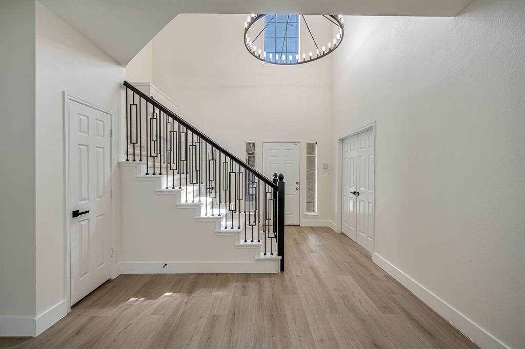 Grand foyer featuring Luxury Vinyl Plank  flooring, a contemporary chandelier, and a prominent staircase with decorative iron railings