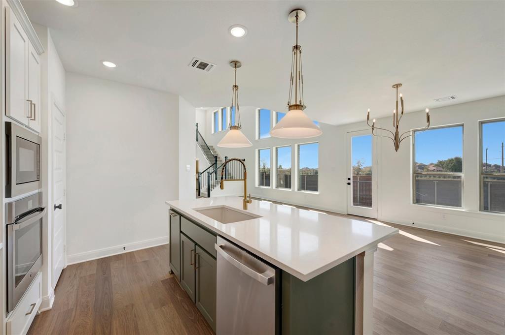Kitchen with a central island featuring a sink and dishwasher, built-in double ovens, wood-finish flooring, and multiple large windows