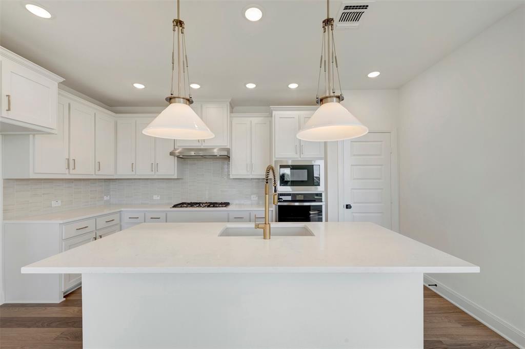 Kitchen featuring a center island with sink, white cabinetry, integrated stainless steel appliances, and wood-finish flooring