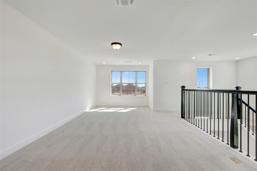 Spacious carpeted area featuring multiple windows, recessed lighting, and a black wrought iron stair railing