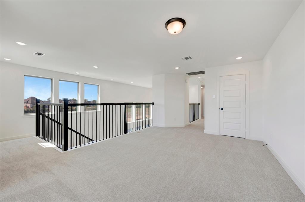 Spacious loft featuring light-toned carpeting, multiple windows, a black metal railing, a panel door, and recessed lighting