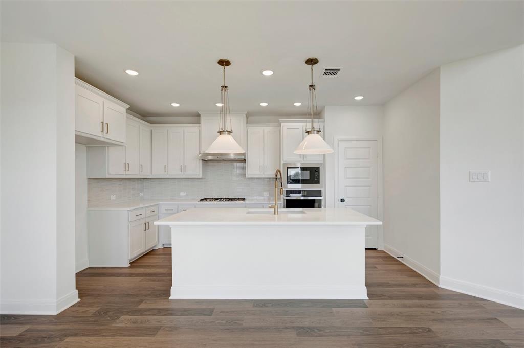 Modern kitchen featuring white shaker cabinetry, an expansive center island, integrated stainless steel appliances, a tile backsplash, and wood-finish flooring