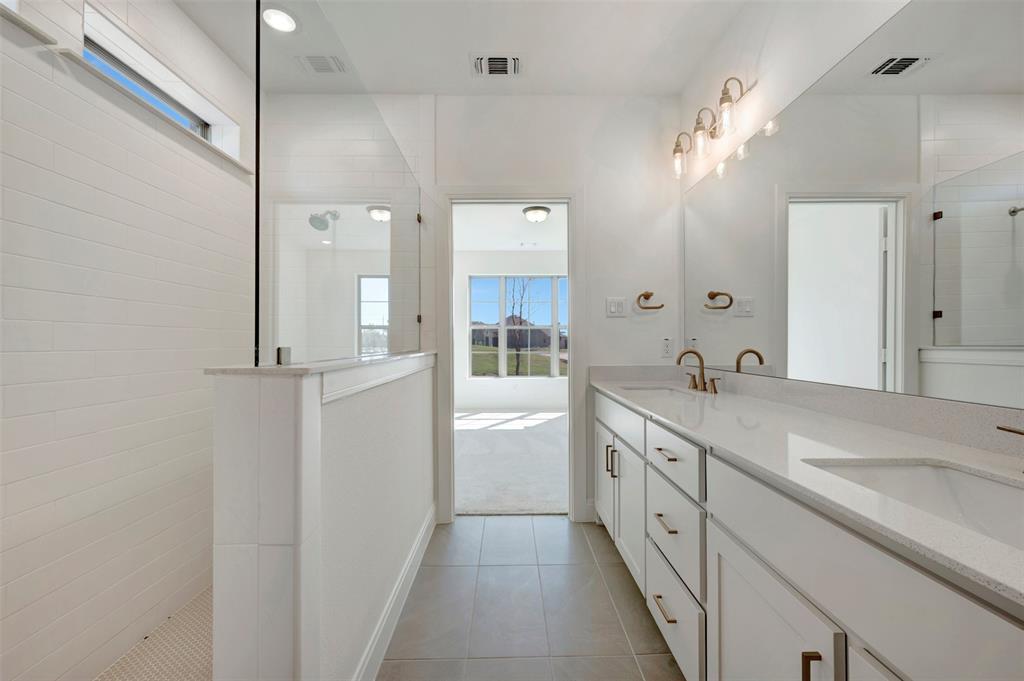 White tile flooring, dual vanities with integrated sinks, white cabinetry, and brushed gold fixtures White tile flooring, dual vanities with integrated sinks, white cabinetry, and brushed gold fixtures