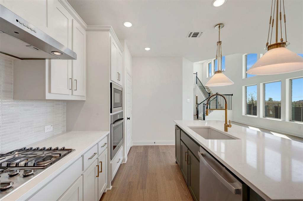 Kitchen featuring white shaker cabinetry, stainless steel appliances, wood-finish flooring, a center island with a sink, and pendant lighting