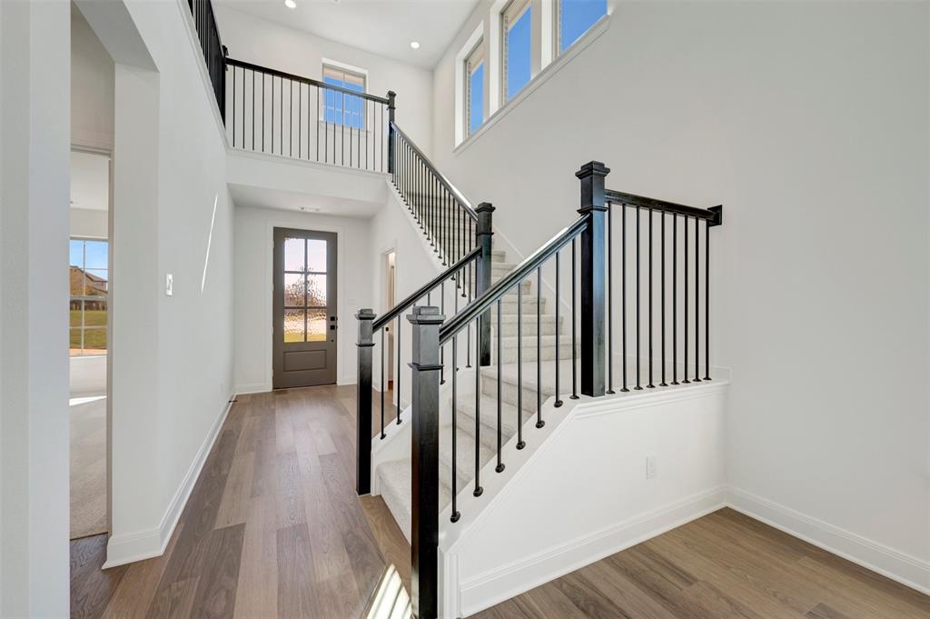 Entryway featuring high ceilings, wood-finish flooring, a contemporary staircase with dark wood newel posts and black metal balusters, and a panel-glass entry door