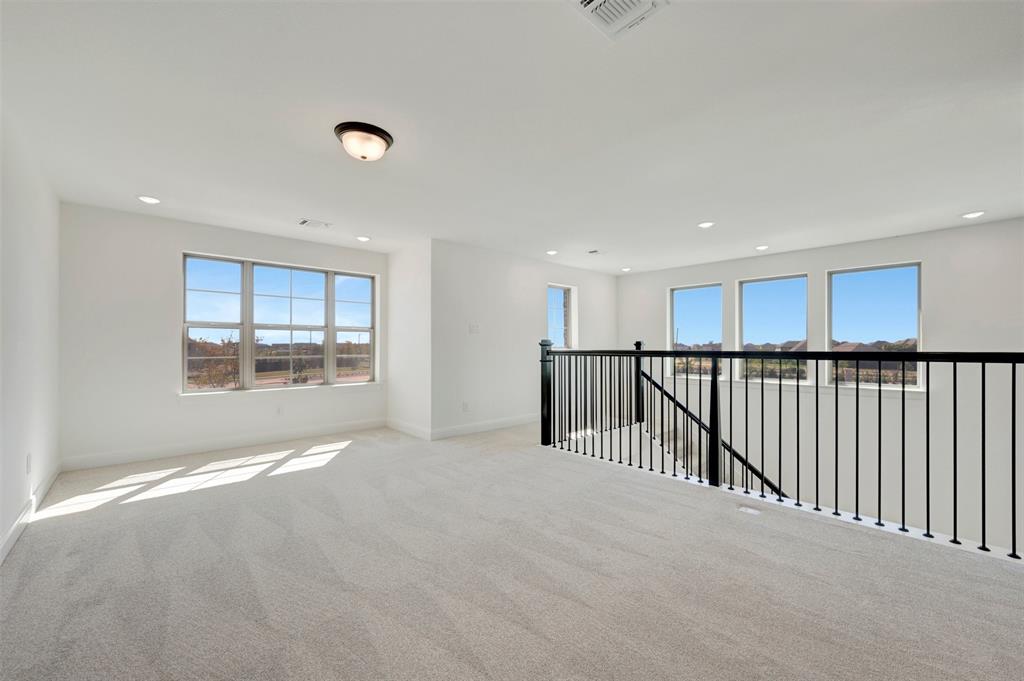 Expansive open loft area featuring light gray carpeting, multiple windows, recessed lighting, and a contemporary black metal railing