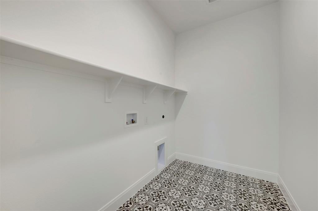 Laundry room featuring a white wall shelf, built-in utility connections, and patterned floor tile