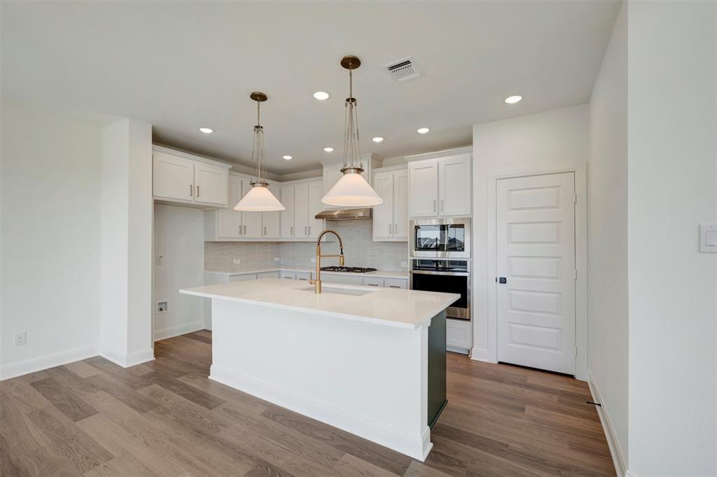 Gourmet kitchen featuring white shaker cabinetry, an island with a light-colored countertop, recessed lighting, and wood-finish flooring