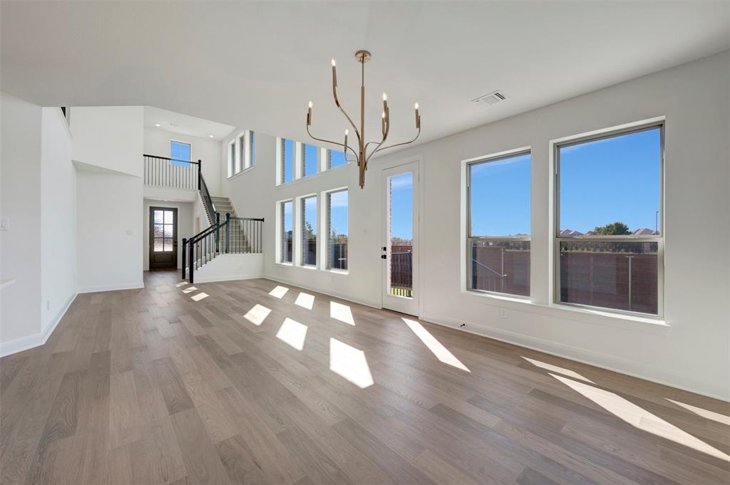 Open-concept living space featuring wood-finish flooring, a two-story ceiling, a modern chandelier, a prominent staircase with metal railings, and multiple large windows