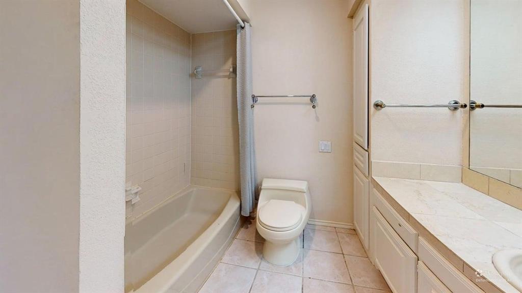 Tiled flooring with a built-in bathtub and shower, complemented by a white vanity with cabinet storage and a mirror