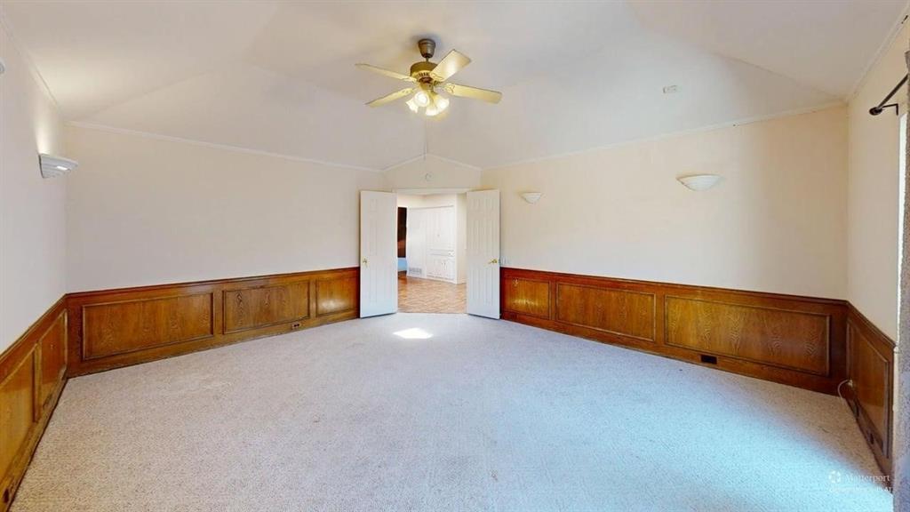 Vaulted ceiling with a ceiling fan, wall-mounted light fixtures, wood-paneled wainscoting, and carpeted flooring