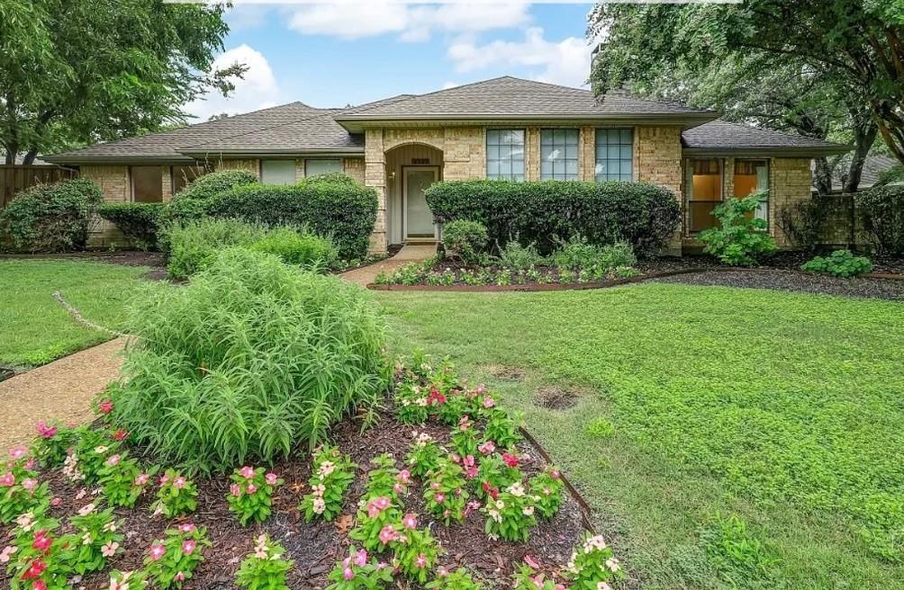 Stone facade home with a shingle roof, mature landscaping, and a concrete pathway Stone facade home with a shingle roof, mature landscaping, and a concrete pathway