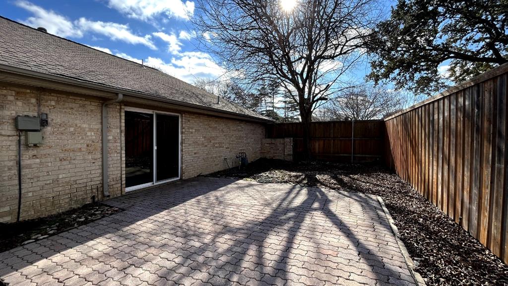 Brick exterior with a paved patio, sliding glass door, and wood privacy fencing