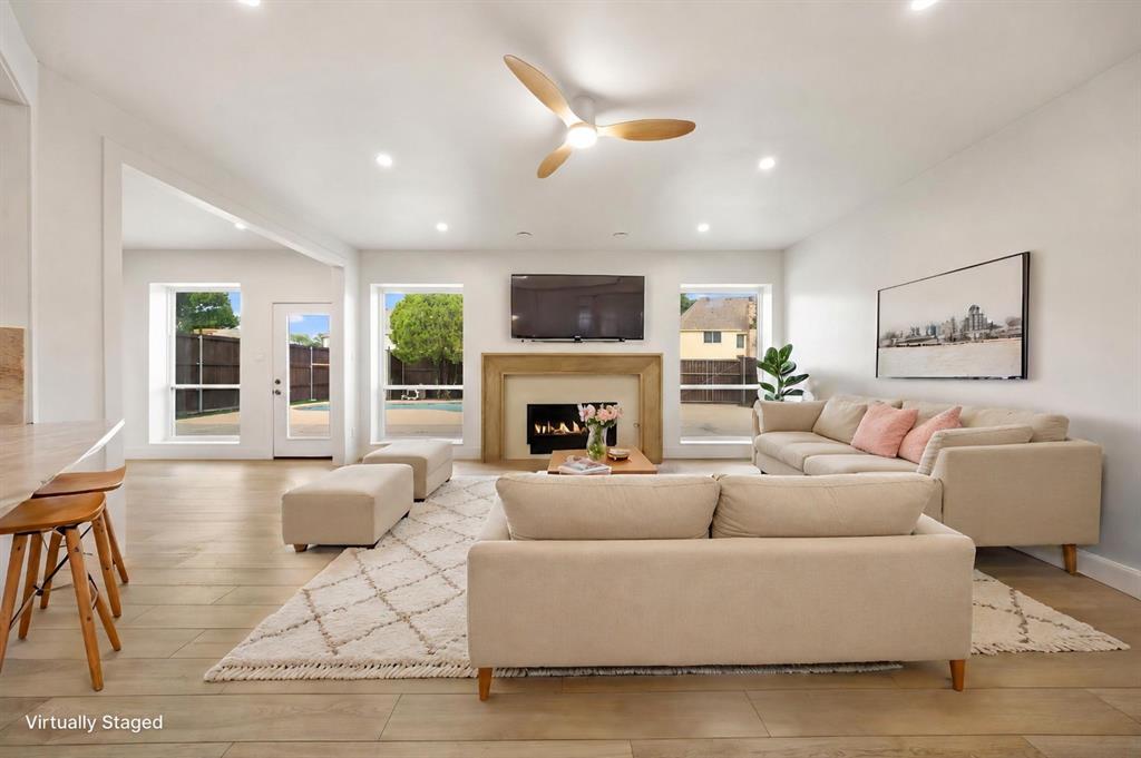 Spacious living area featuring a fireplace with a stone surround, recessed lighting, wood-finish flooring, and a contemporary ceiling fan Spacious living area featuring a fireplace with a stone surround, recessed lighting, wood-finish flooring, and a contemporary ceiling fan